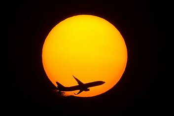 Пассажирский самолет пролетает на фоне заходящего солнца в Шанхае.